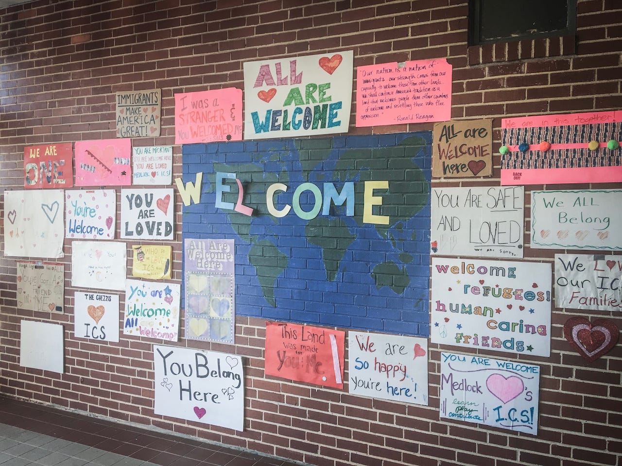 Handmade posters welcoming newcomers hang on a brick wall.