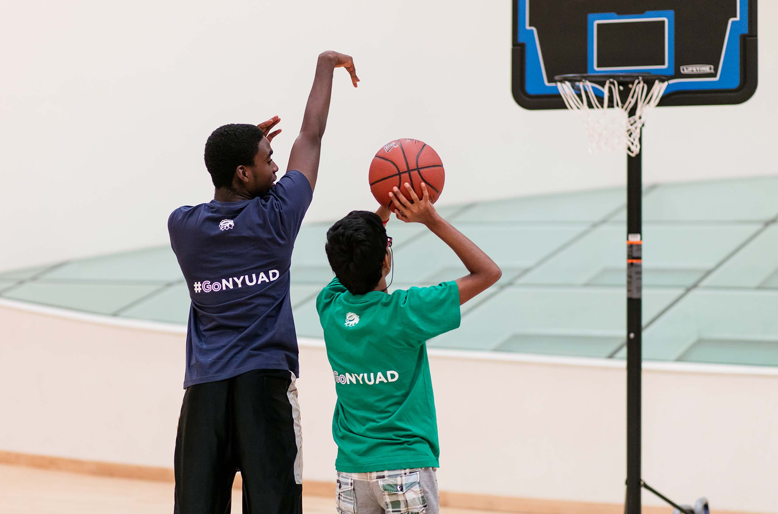 NYU Abu Dhabi student demonstrating to a child how to properly shoot a basketball