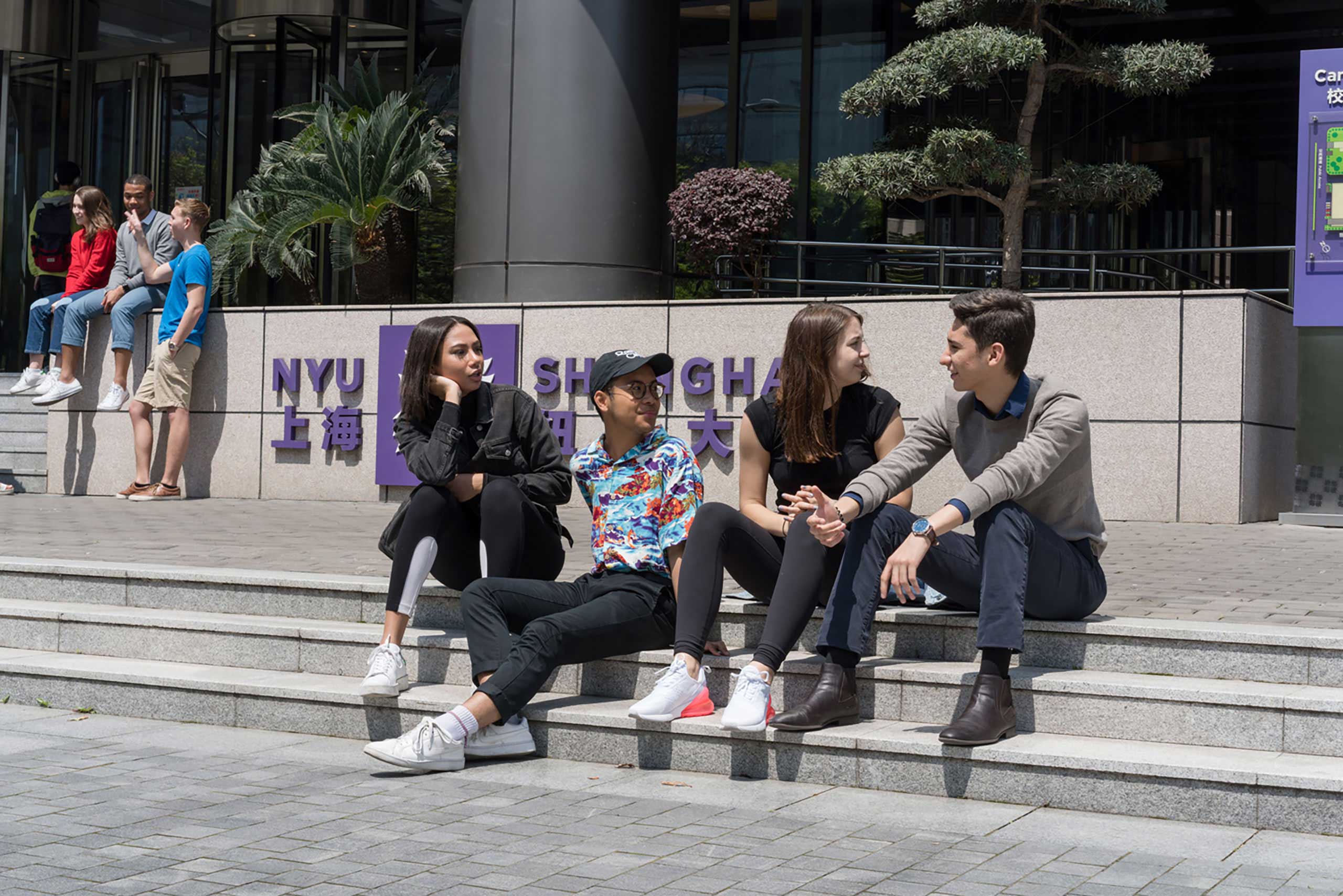 Students sitting on steps in front of NYU Shanghai's main entrance
