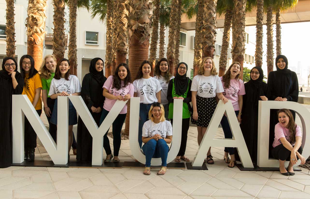 A group of women from Next Gen sit on an NYU Abu Dhabi sign.