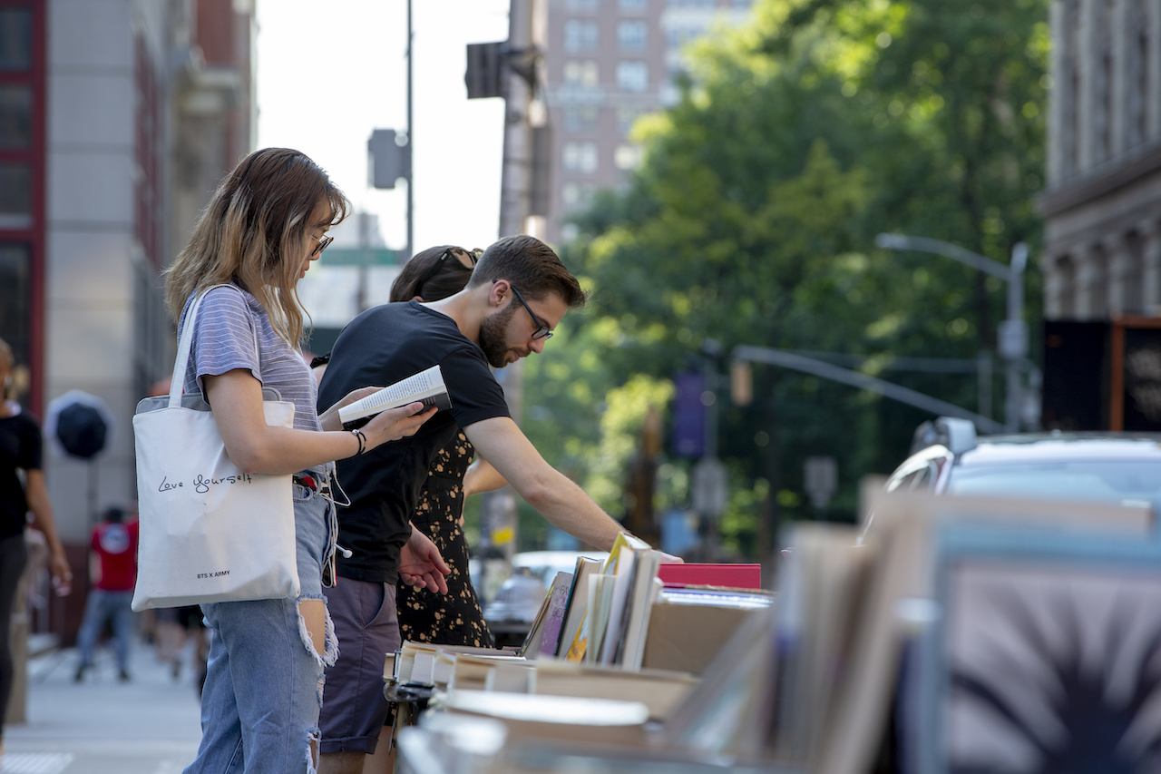 [Two people browse books at a street vendor table.]