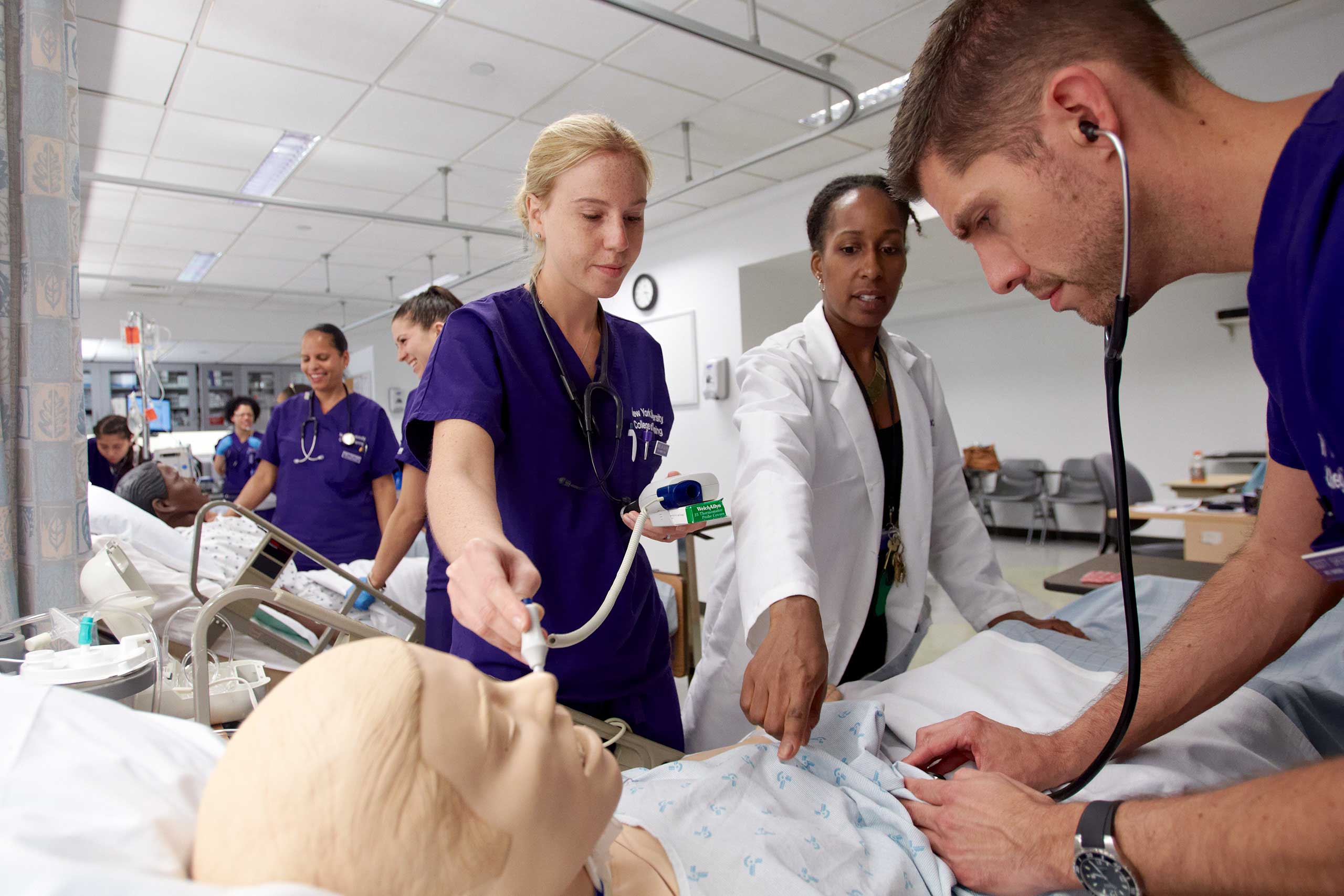 Students with a Global Public Helath major combined with Nursing being taught by a professor how to use a stethoscope on a medical mannequin