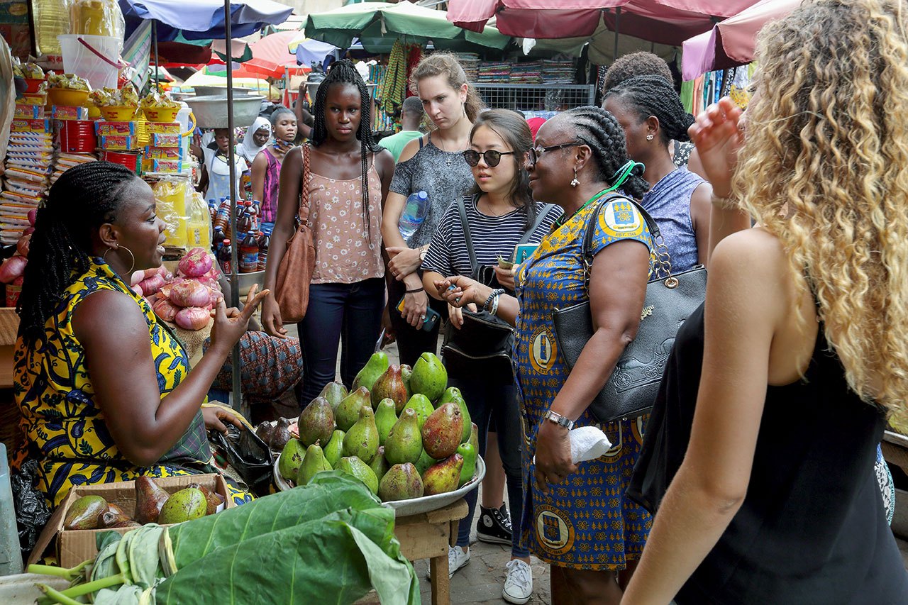 A group of students learning about local food and nutrition at an outdoor fruit market in Accra, Ghana