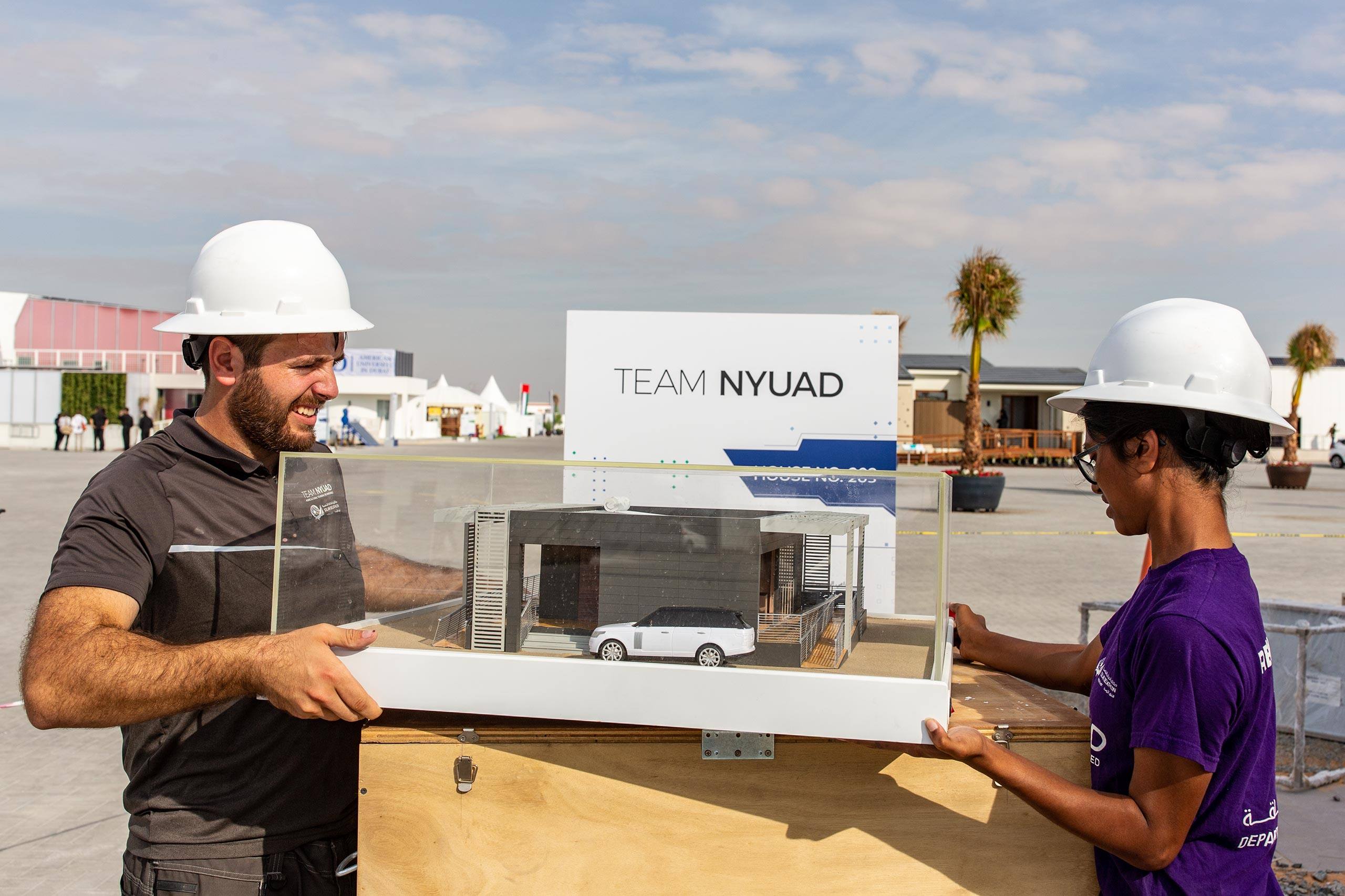 Two students hold up an architectural model of their solar house.