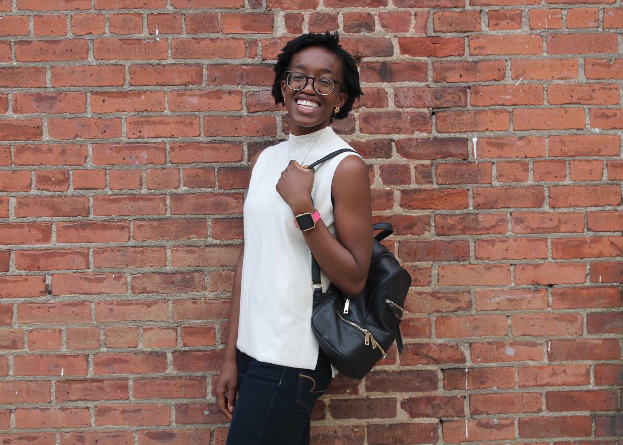 Camille Aké posing against a brick wall.