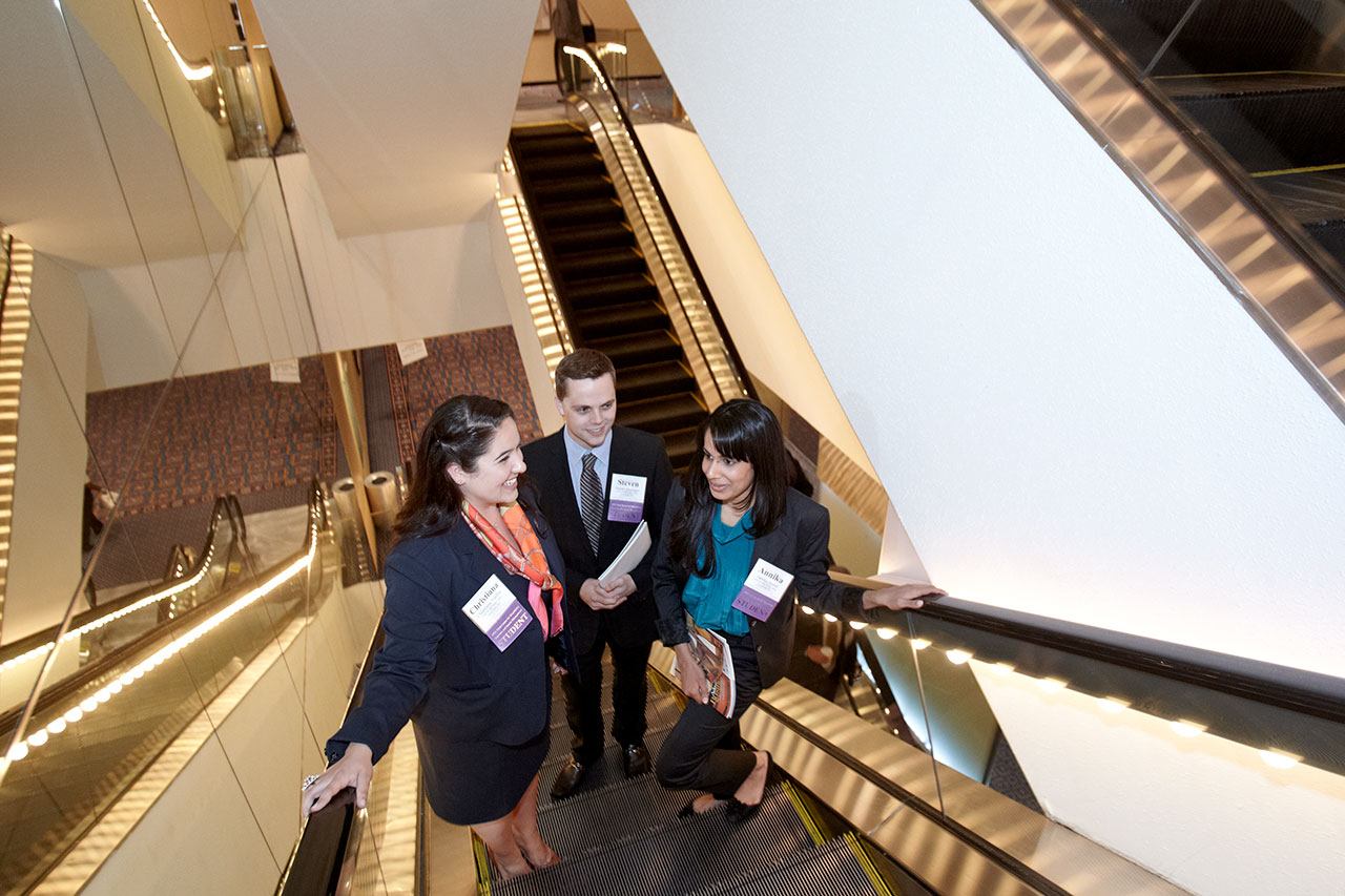 Three students ascending a hotel lobby escalator. 
