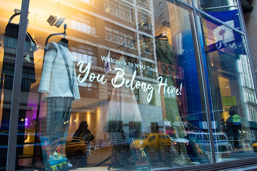 NYU Tisch window showcasing costumes with a decal that reads, “You Belong Here!”