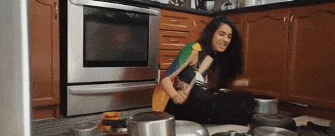 A woman happily banging pots and pans in the kitchen.
