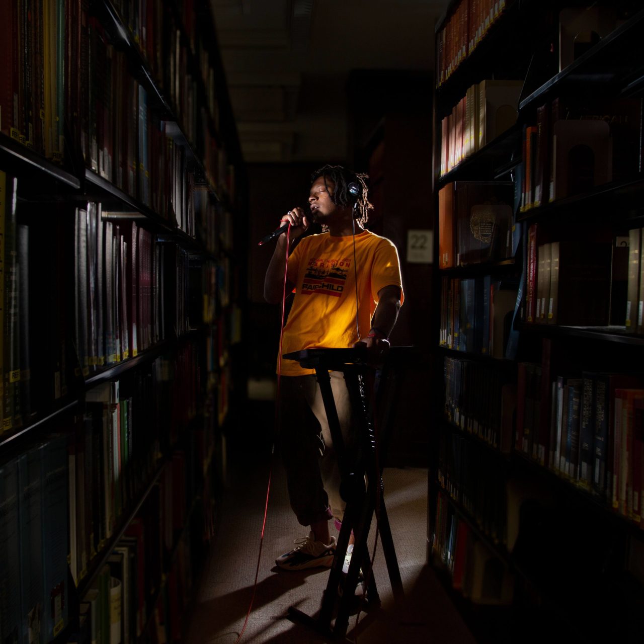 Student Marcus Harley performing into a mic behind equipment while standing in between library book stacks.