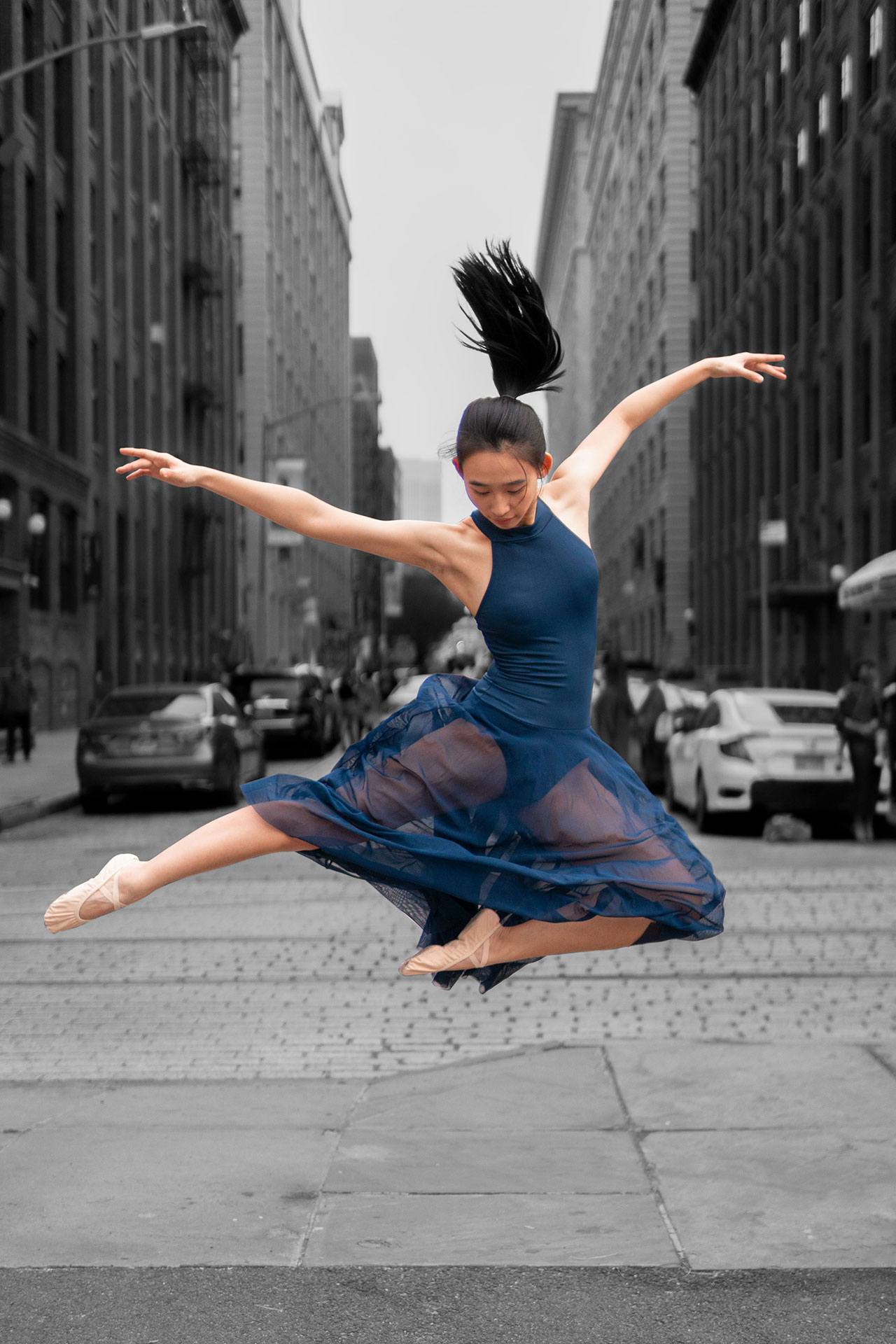 Dancer leaps in the air in the middle of a cobblestone street in Brooklyn.