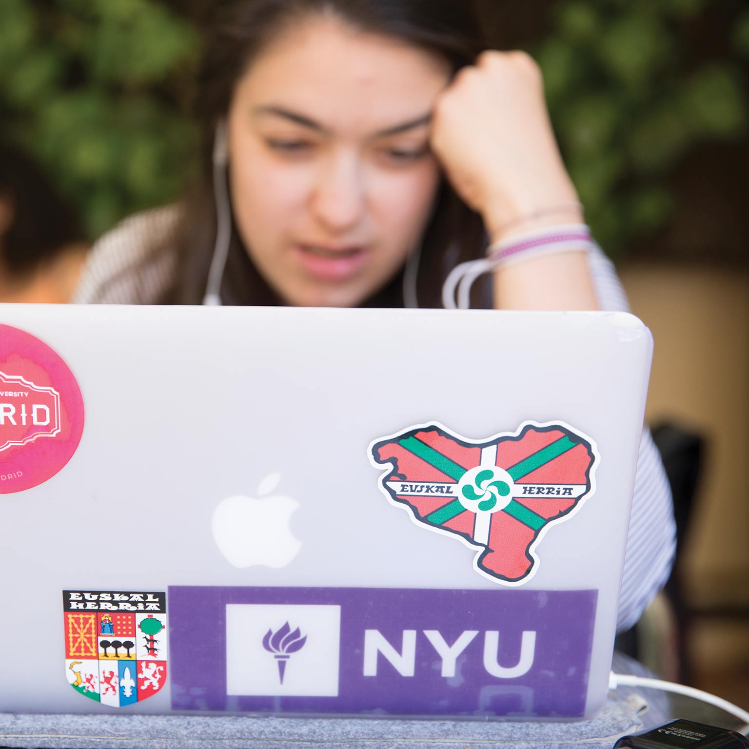 A student looking at laptop with NYU sticker visible on back.