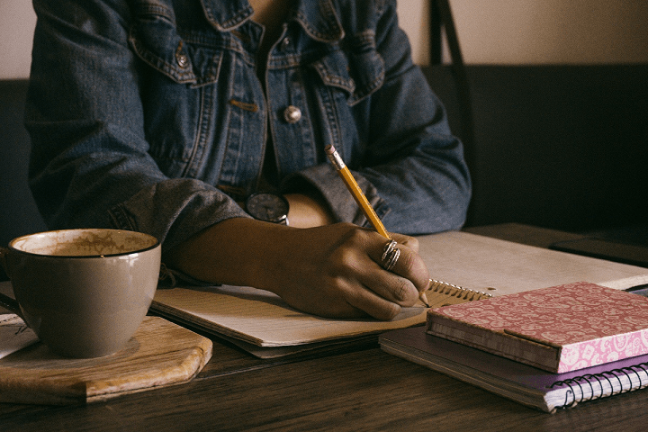 Close-up of a womanʼs hand holding a pencil, writing in a notepad.