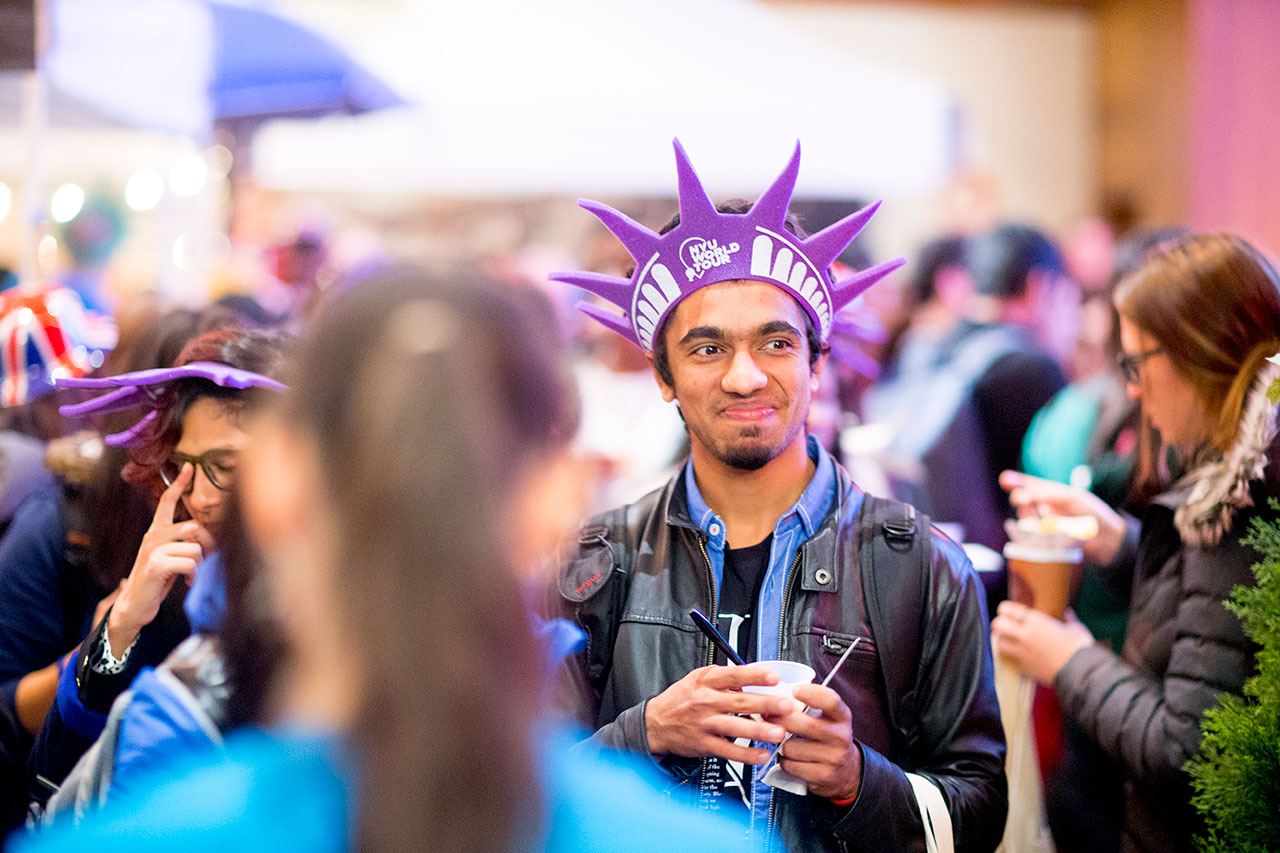 Student standing in a crowd, wearing a Statue of Liberty hat, and smiling.