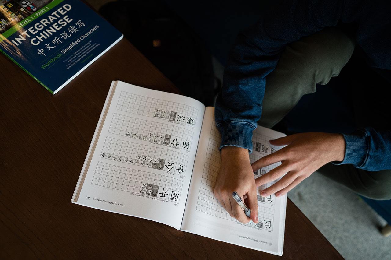 Hands writing Chinese characters in a language learning book.