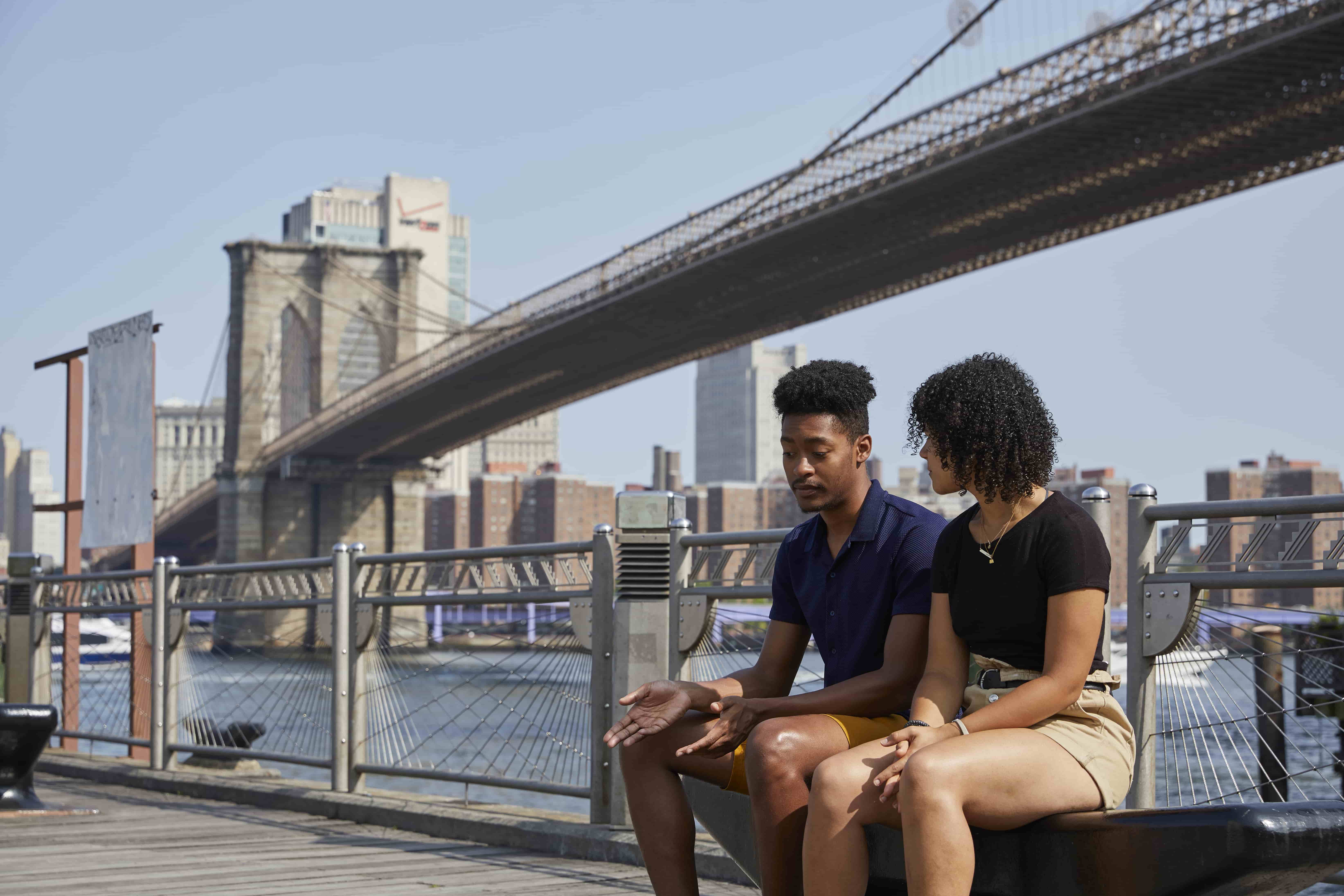 Two students sitting on bench near the Brooklyn Bridge.