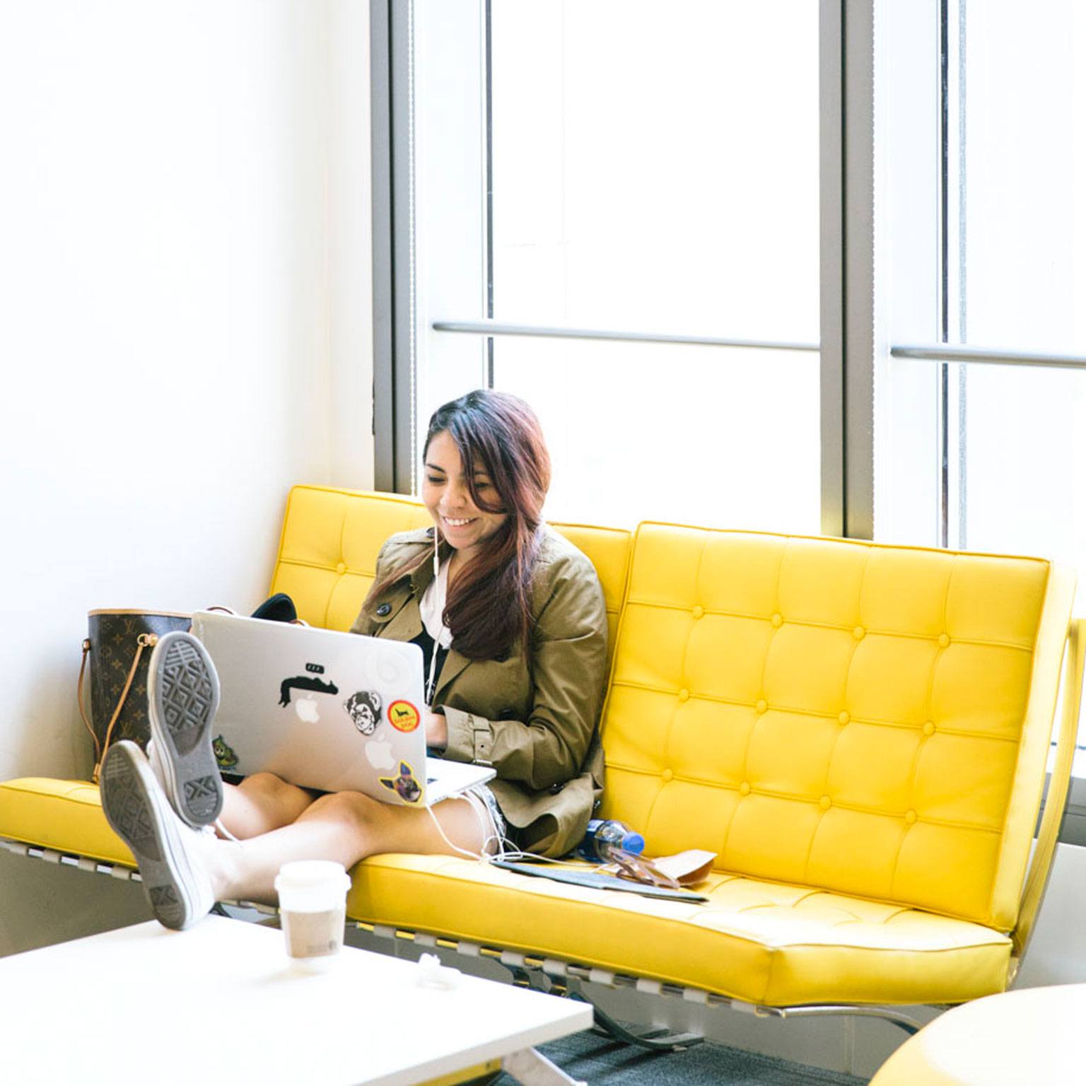 Student sitting on a yellow couch, working on her laptop.