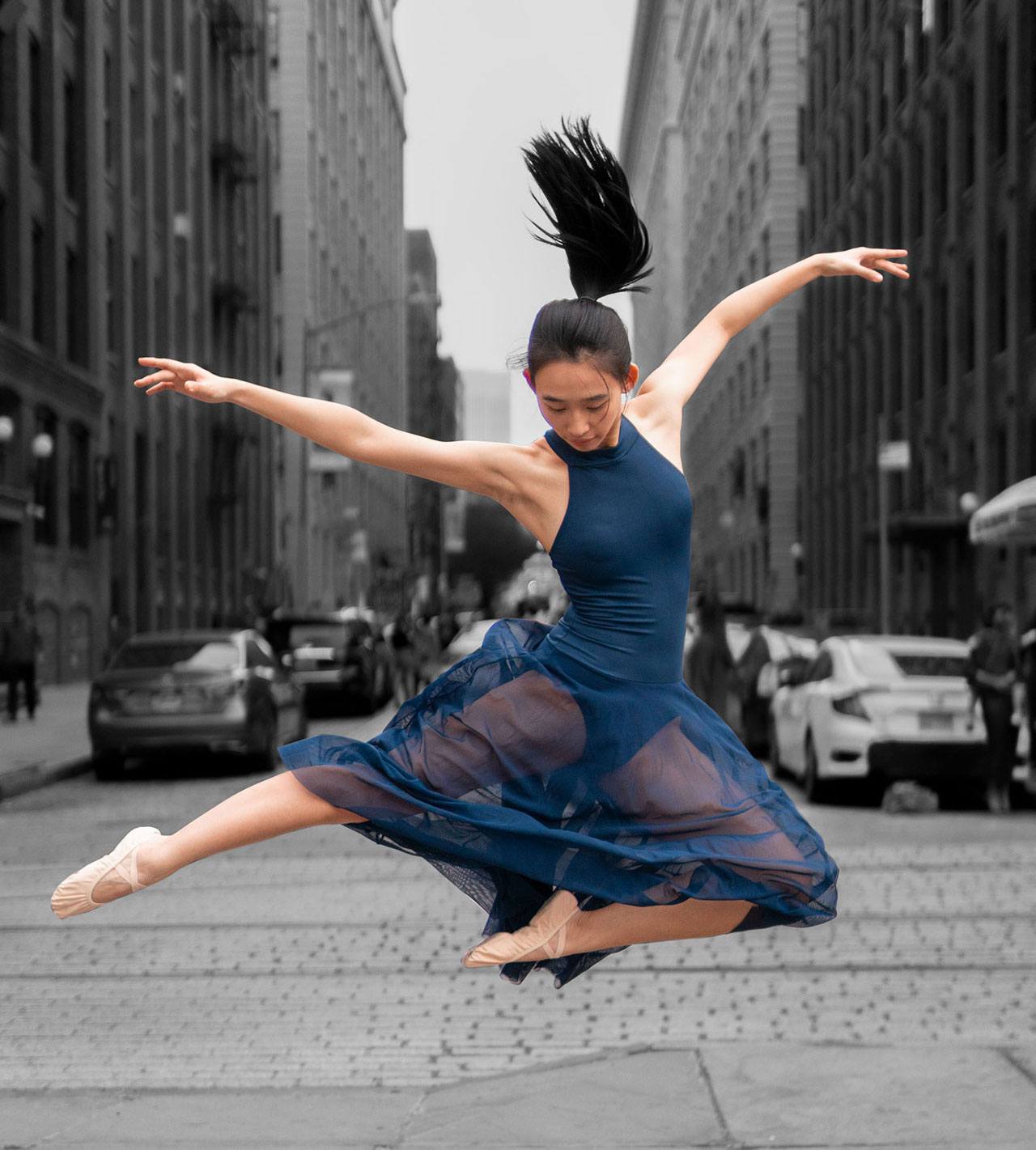Dancer leaps in the air in the middle of a cobblestone street in Brooklyn.