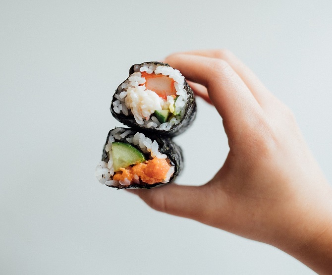 A hand holding two sushi rolls.