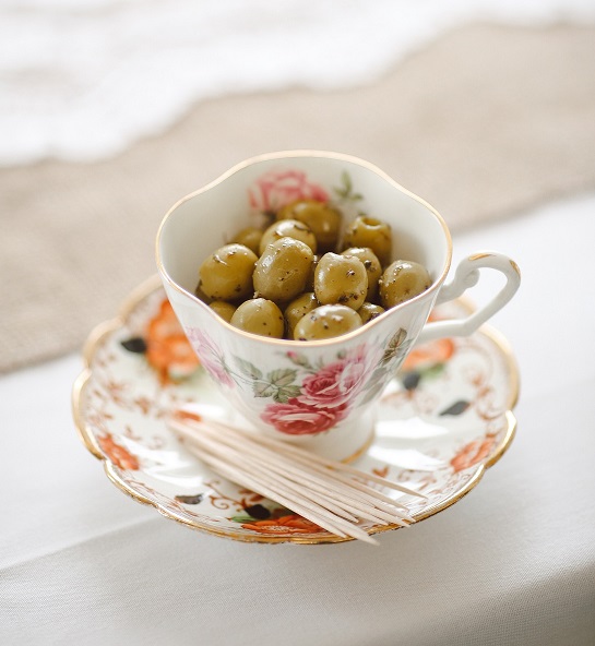 Green olives in a teacup with toothpicks on the saucer.