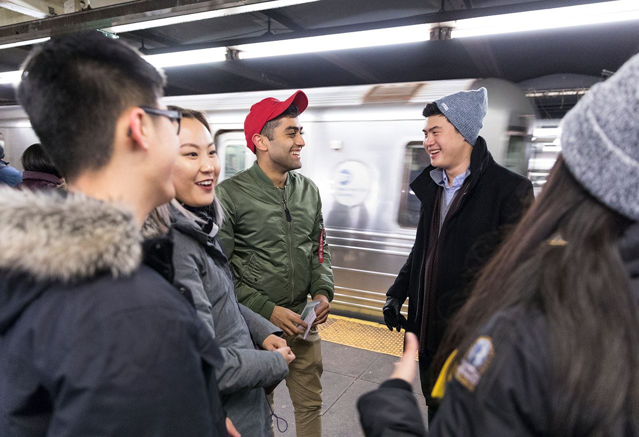 A group of students standing in a circle and talking on a NYC subway platform.