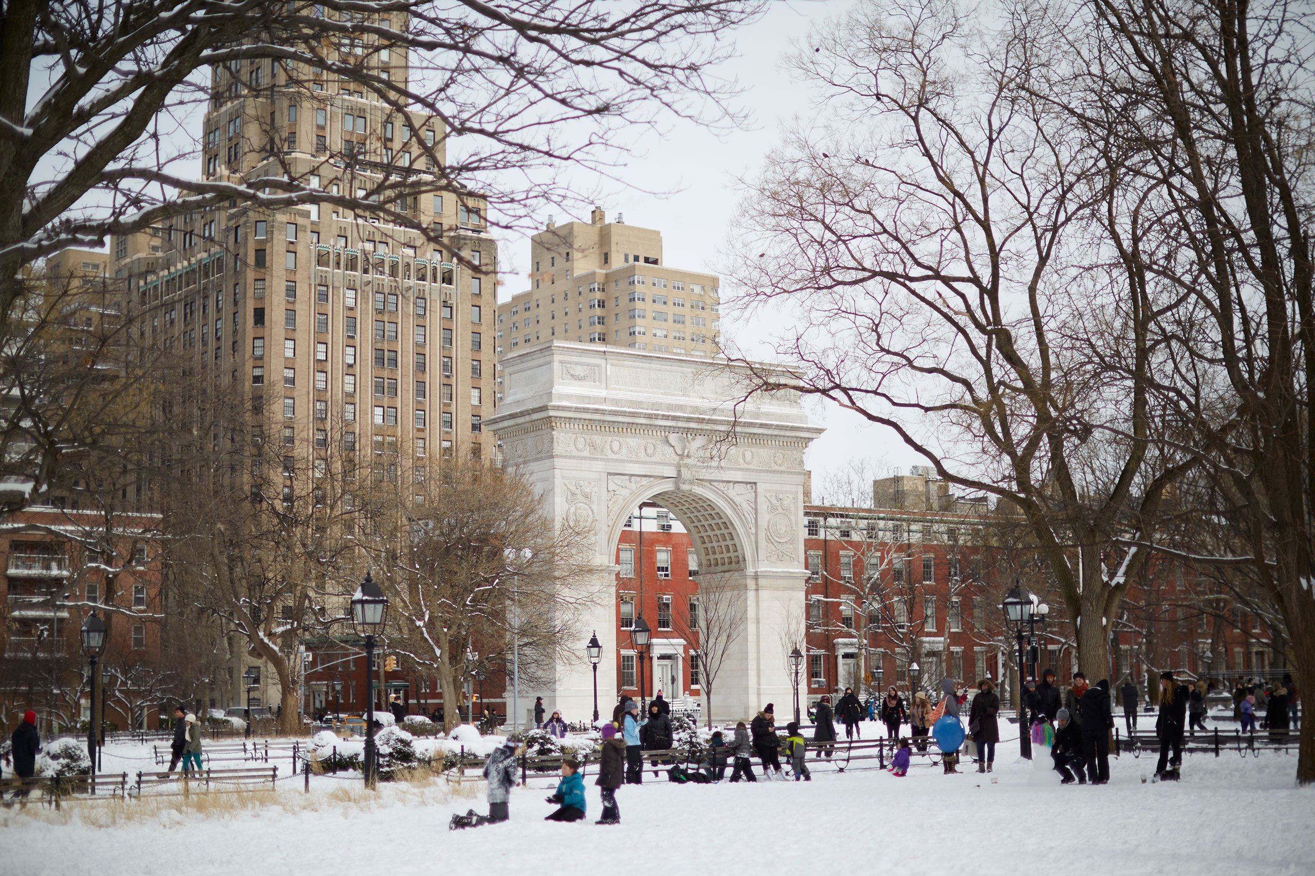 Groups of people playing in the snow in front of the arch at Washington Square Park.
