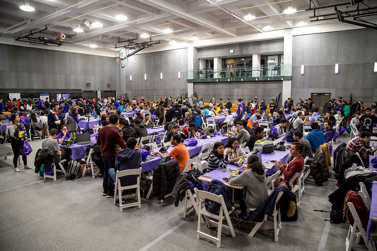 A large group of HackNYU participants sitting at long tables.