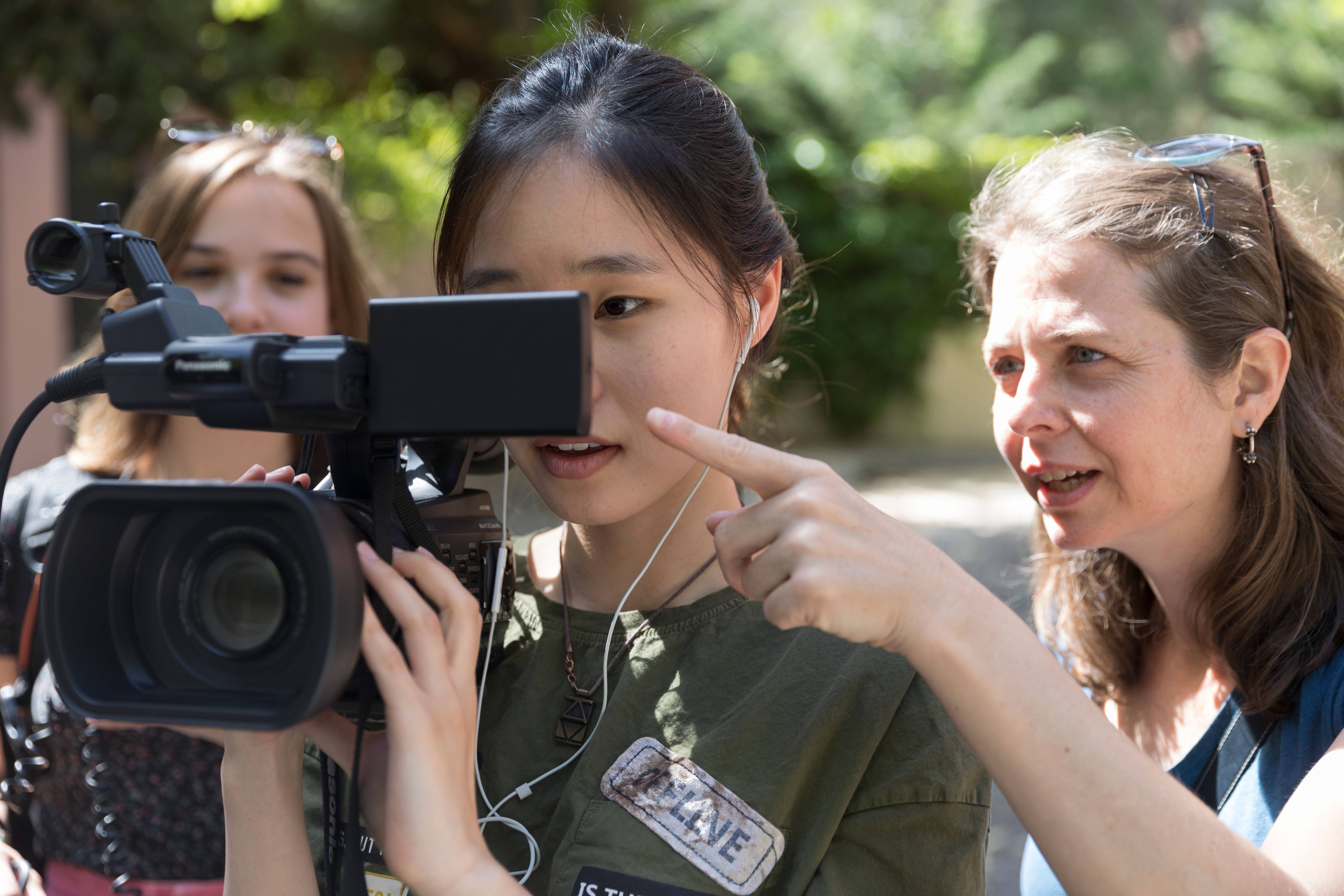 A student holding a camcorder while a professor points at the viewfinder.