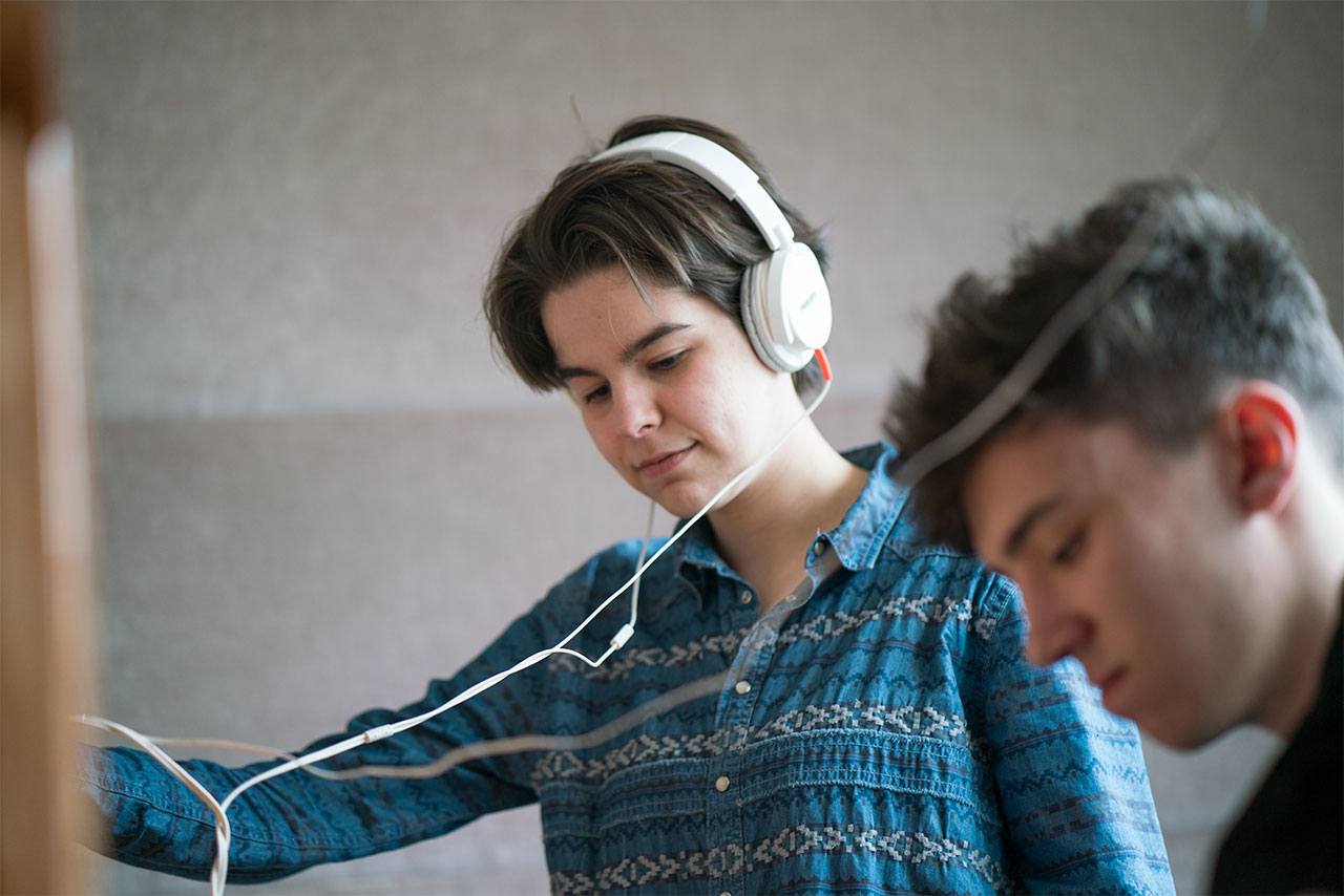 One student wearing headphones listen to music, while another student plays the piano.