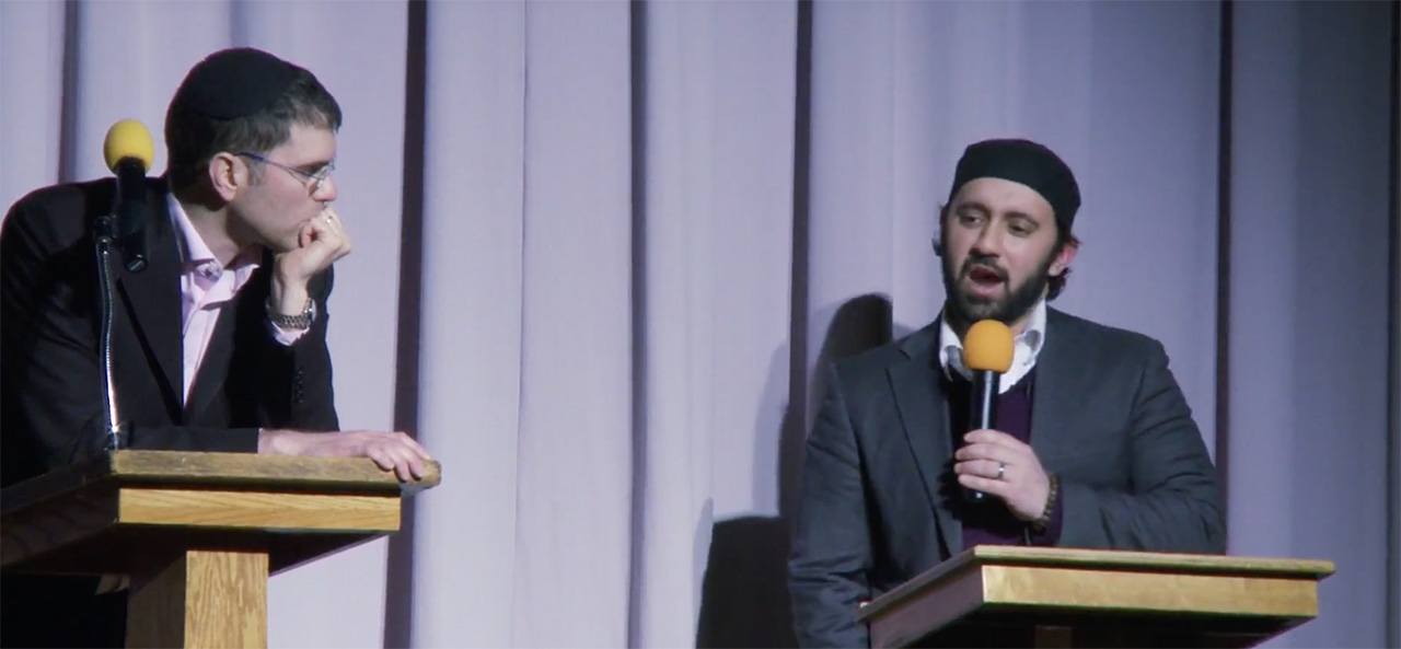 Imam Khalid Latif and Rabbi Yehuda Sarna speaking on stage at an event.