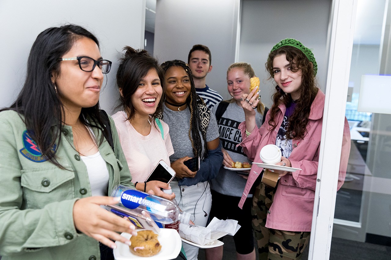 A group of students smiling and eating pastries.