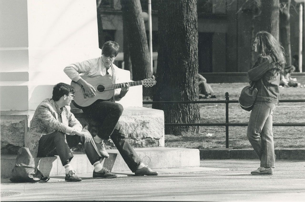 A throwback of three students in Washington Square Park near the arch. One student is holds a guitar.