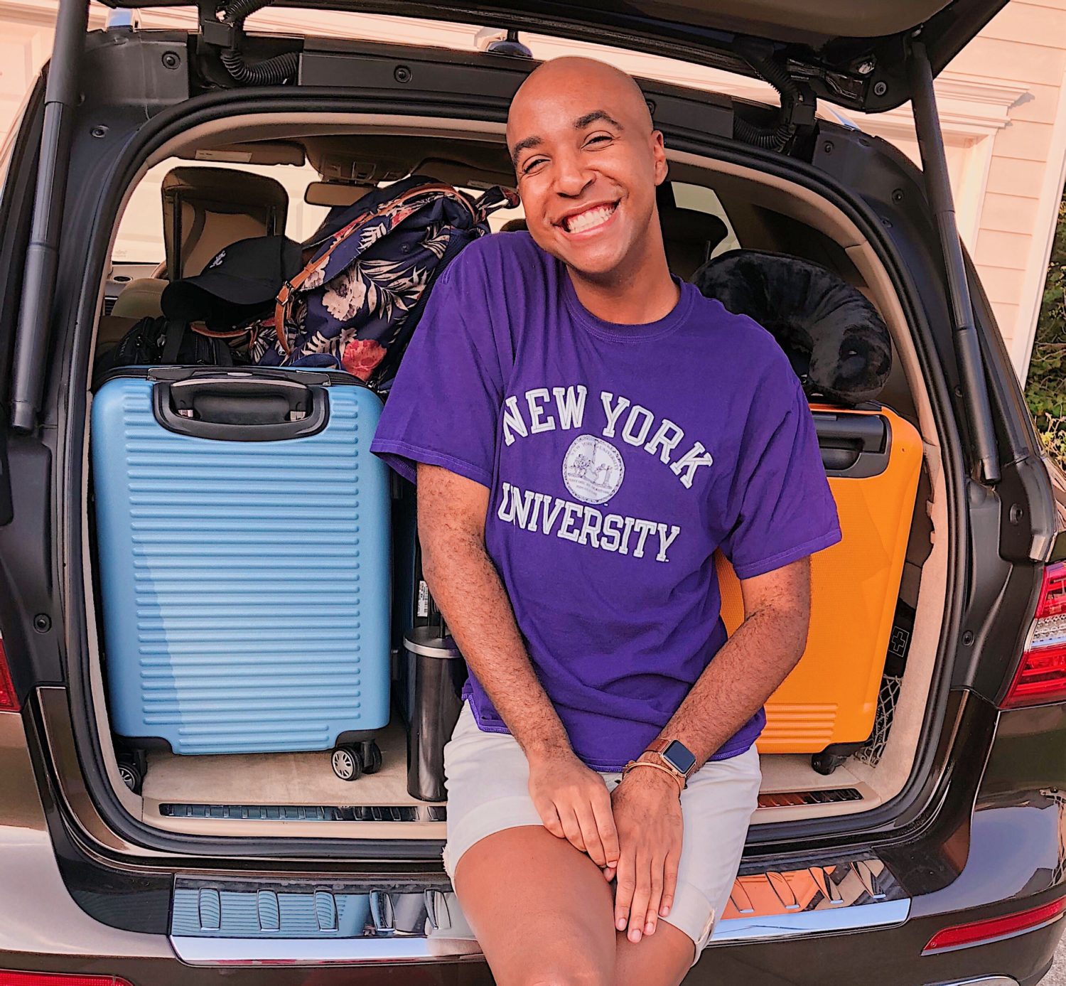 An NYU student sitting in front of suitcases in the truck of a car.
