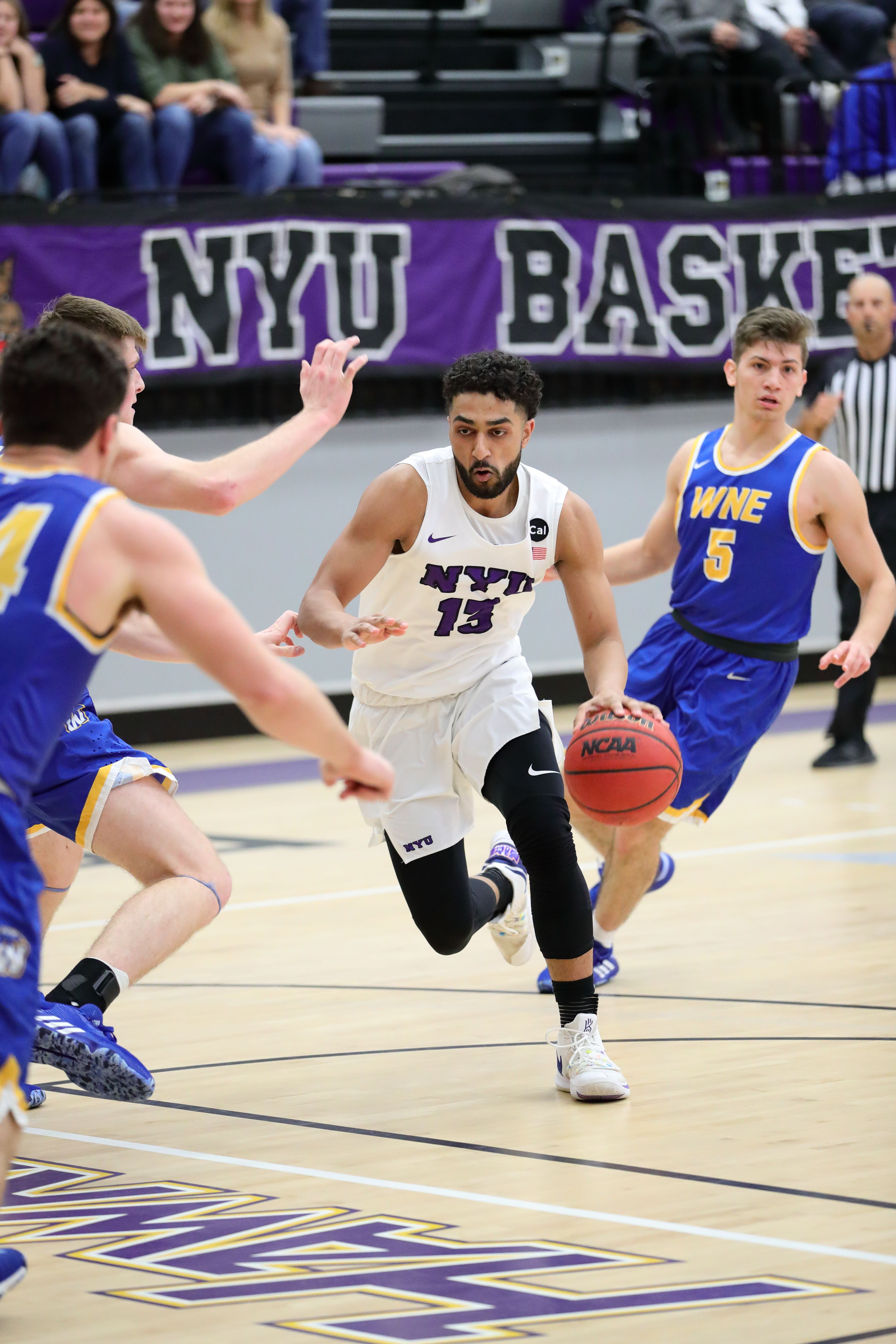 NYU men's basketball player dribbles the ball down the court