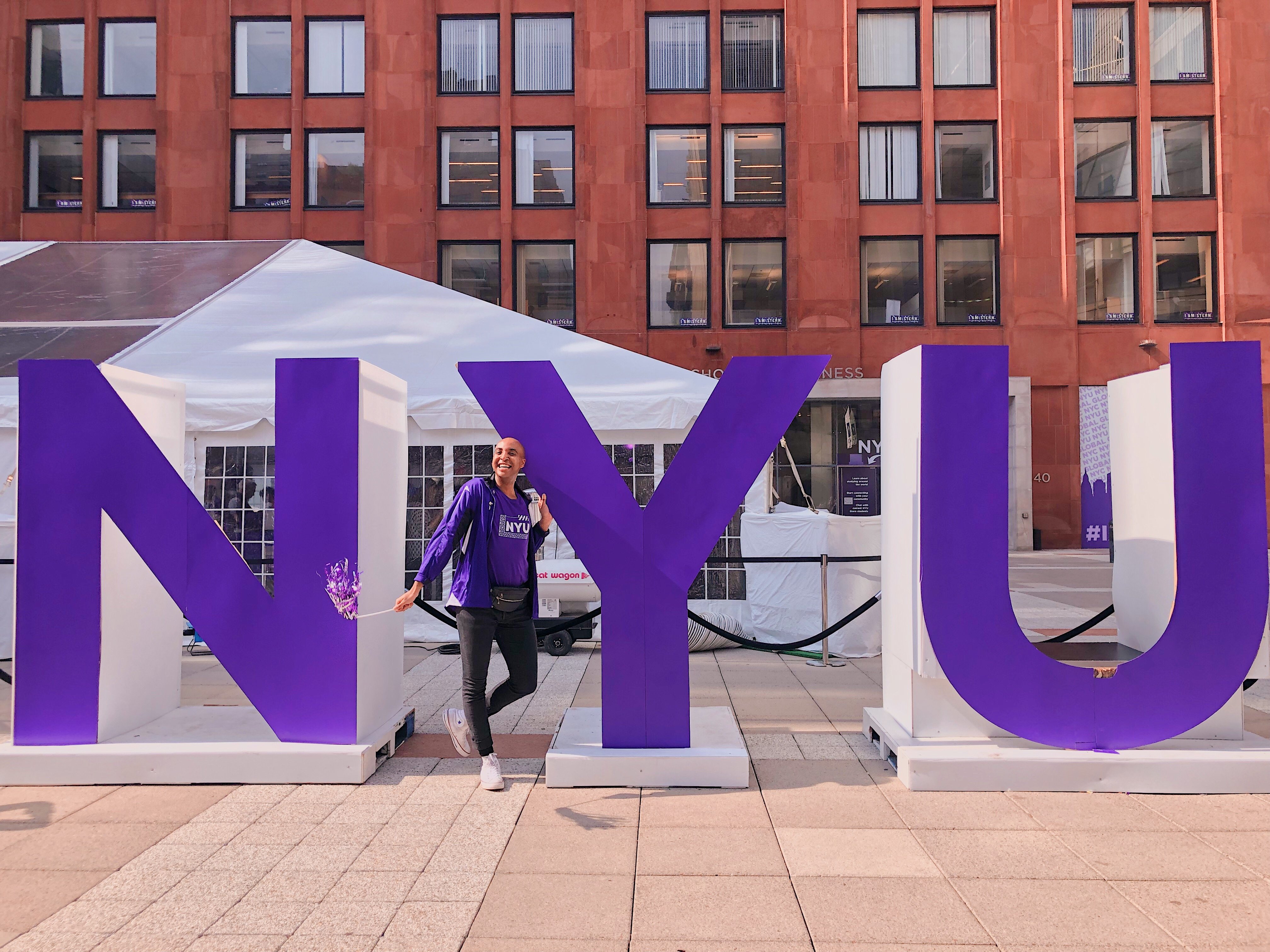 A student standing in front of an NYU sign.