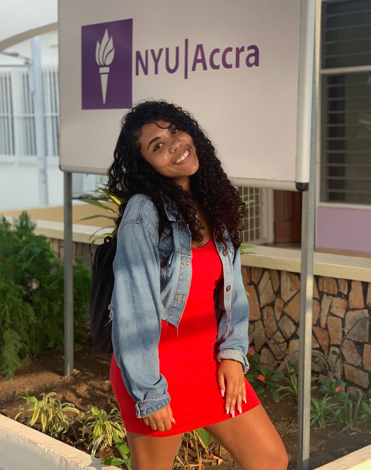 Elizabeth Pontes posing for a photo infront an NYU Accra sign
