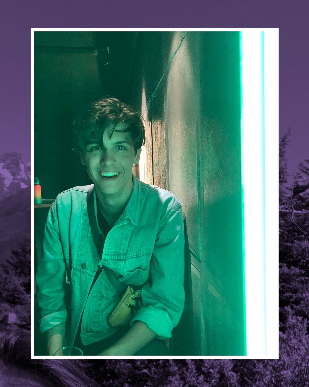 NYU Steinhardt student Justin Kipp posing in front of a vibrant green neon light.