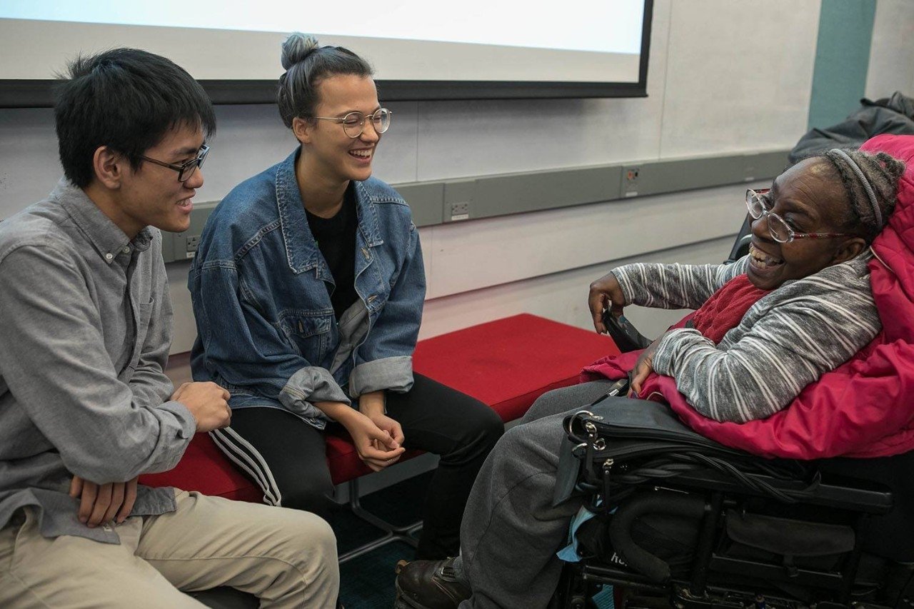 Two students with a guest consultant who is in a wheelchair.