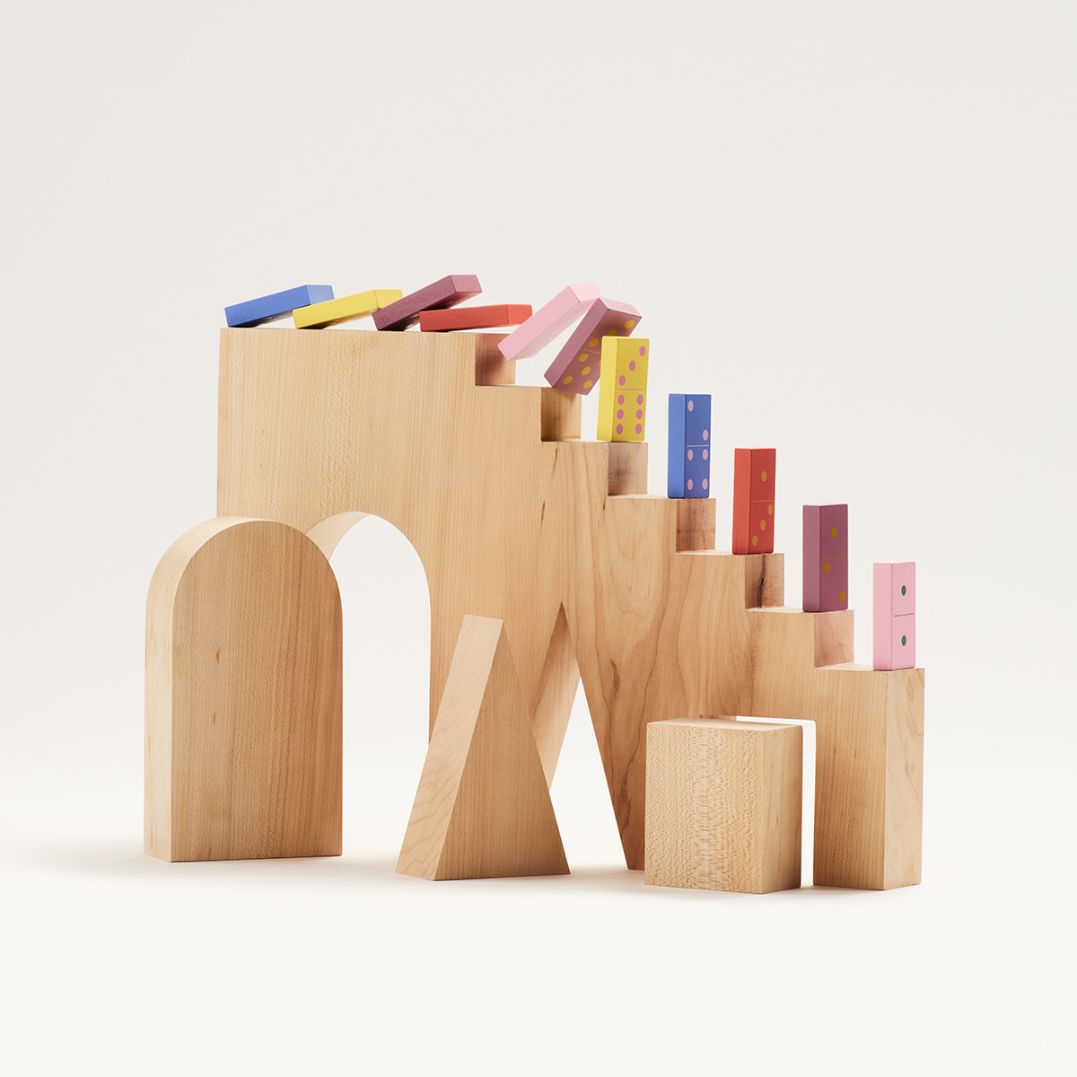 Still life of colorful dominoes falling down a wooden staircase made of blocks.