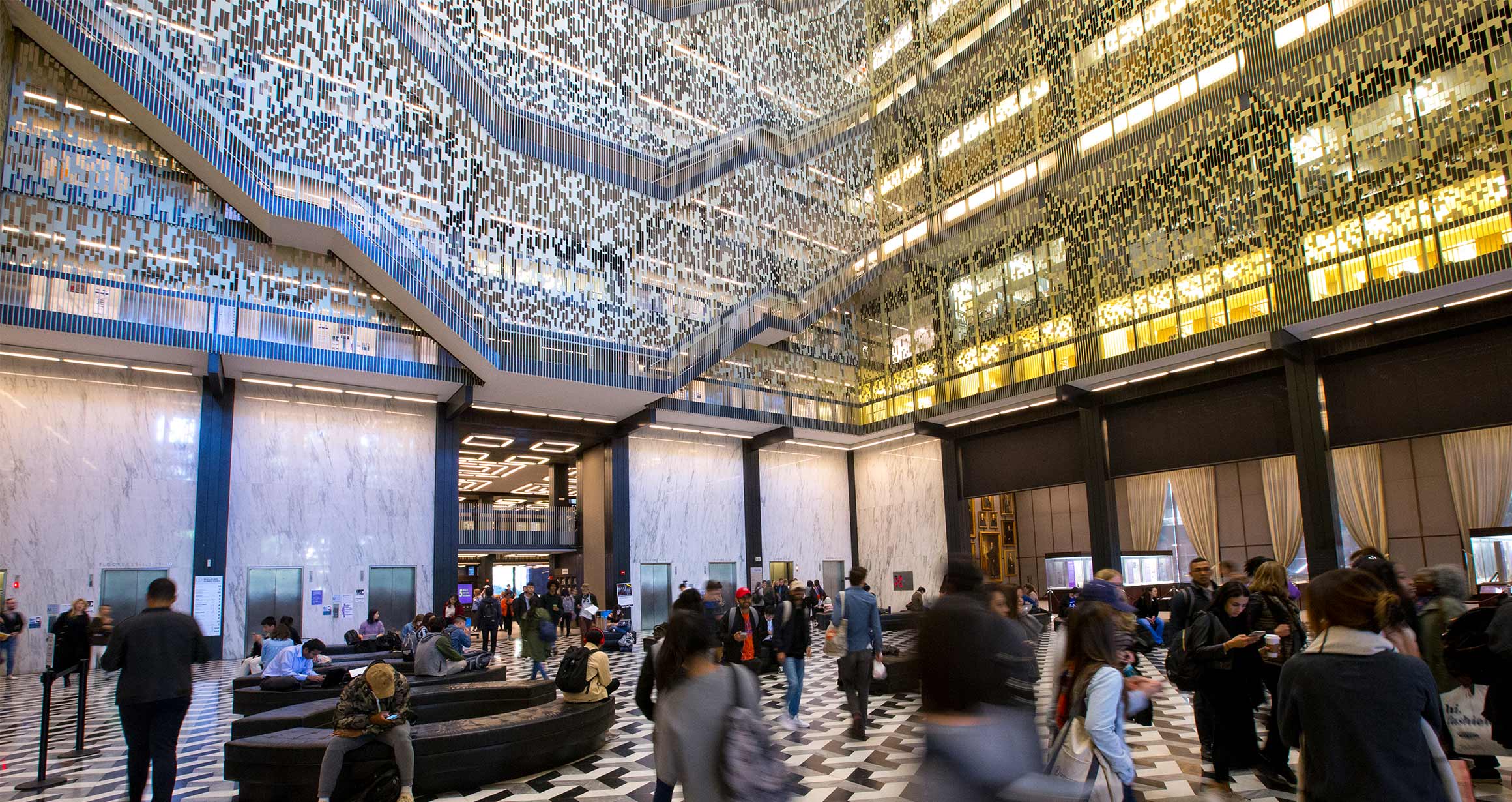 The main lobby of the bobst library and many students can be seen moving about.
