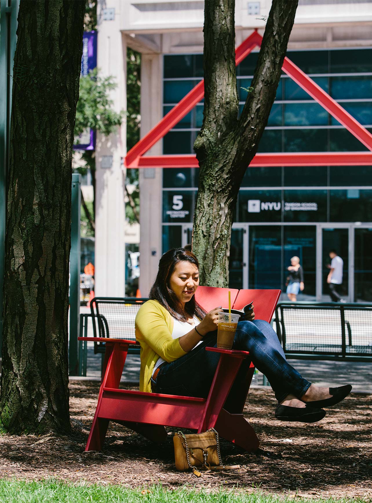 A student sits in the sun reading a book in the commons