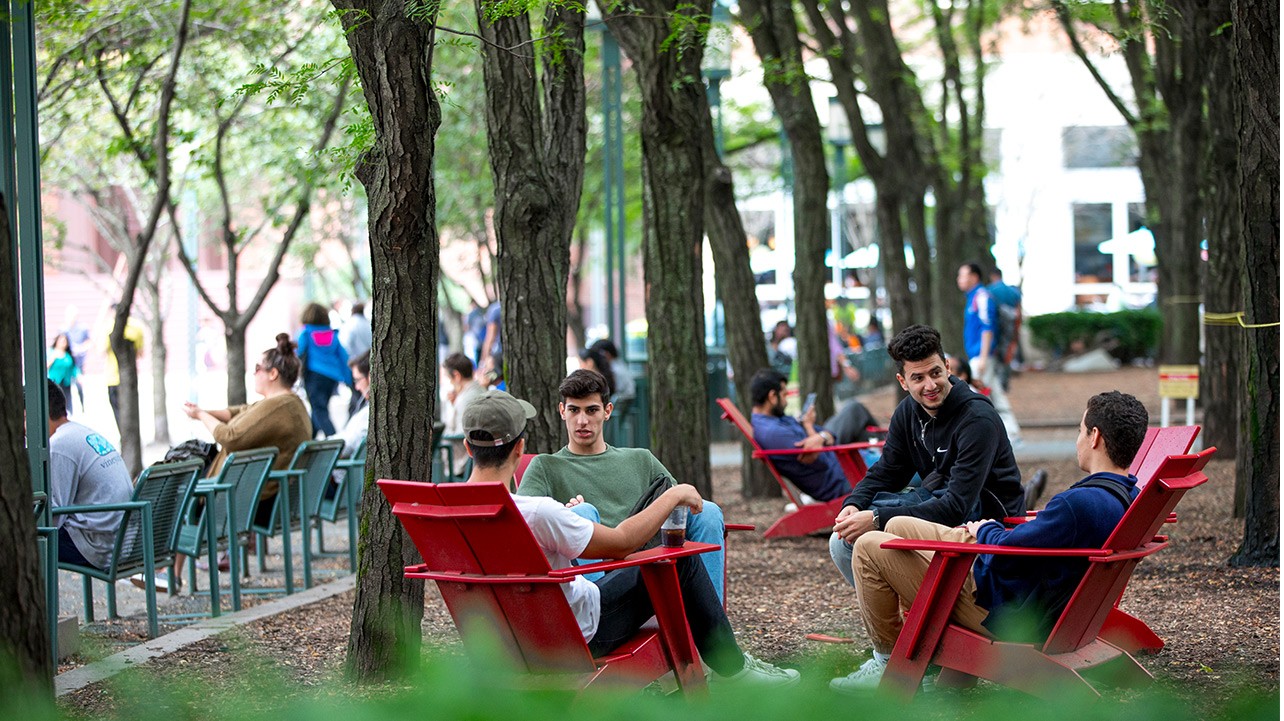 A group of students sit in red wooden chairs in metrotech commons