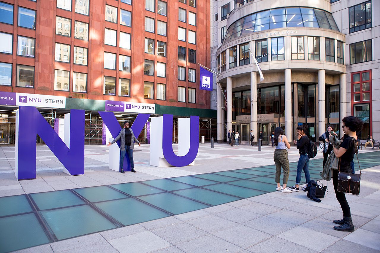 Students posing in front of large NYU sign.