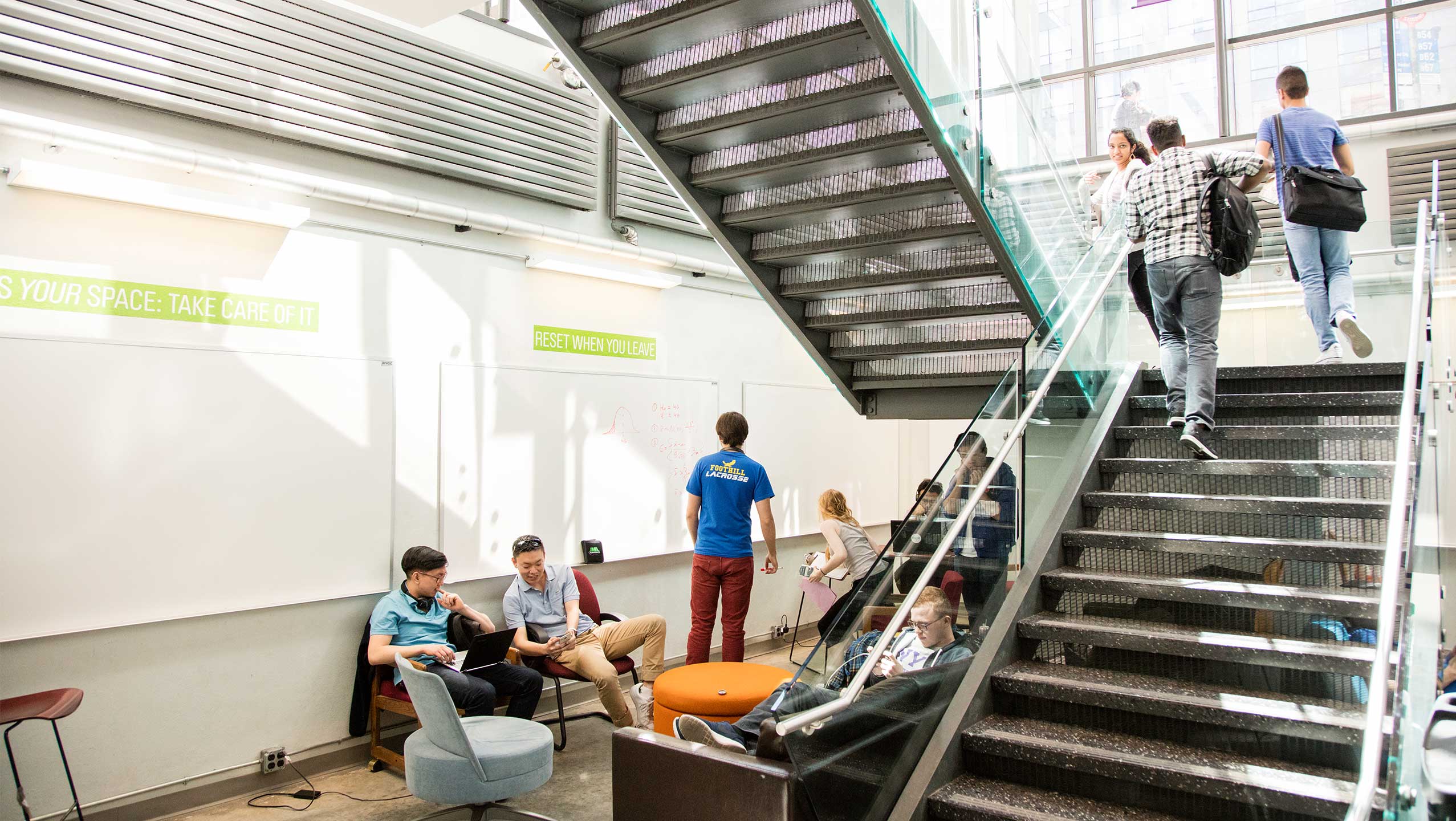 Students can be seen sitting in a lounge and walking up the steps within the Jacobs building.