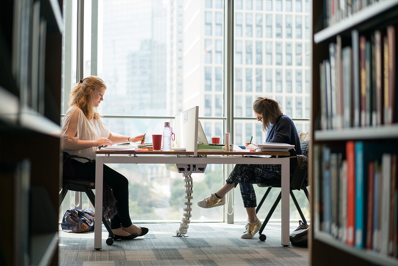 Two students studying at a table in the library.
