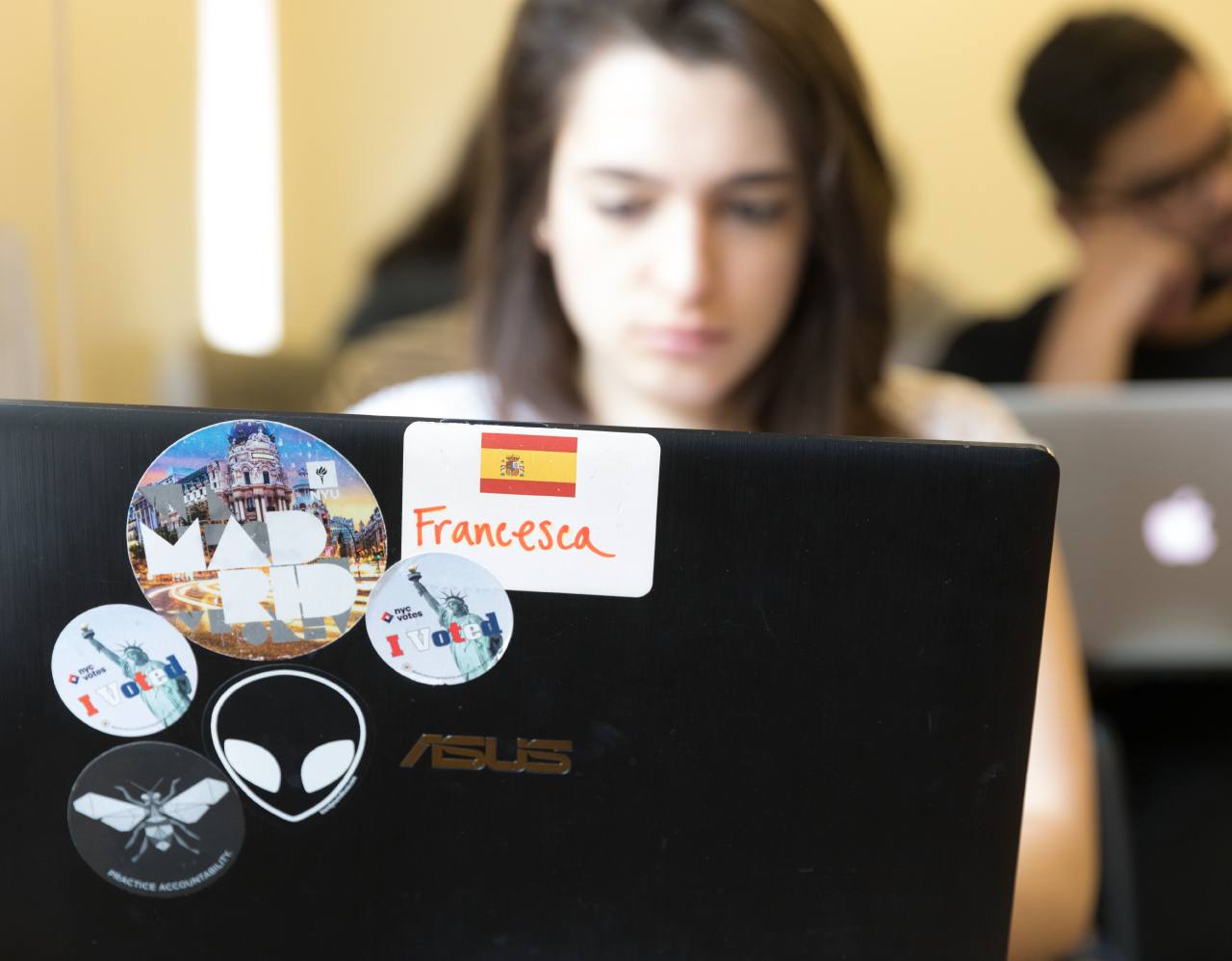 A student on their laptop in class. Their laptop is covered with stickers.