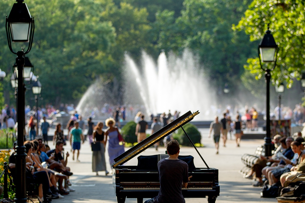 A piano performer playing to a large group of people in the park.