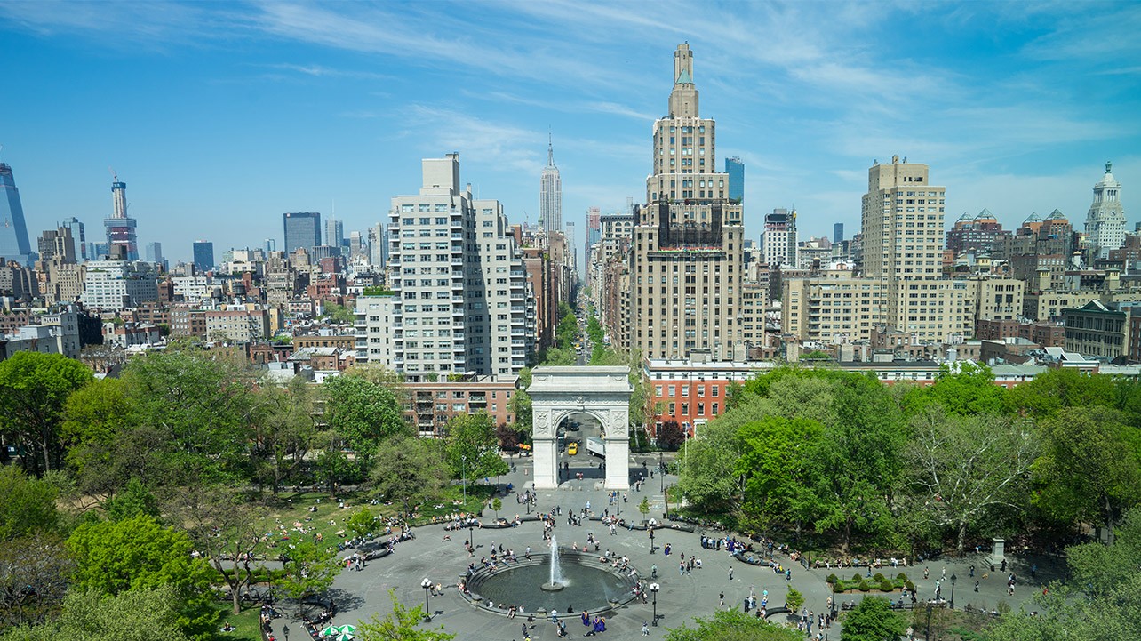 A wide shot of Washington Square Park with the New York Skyline