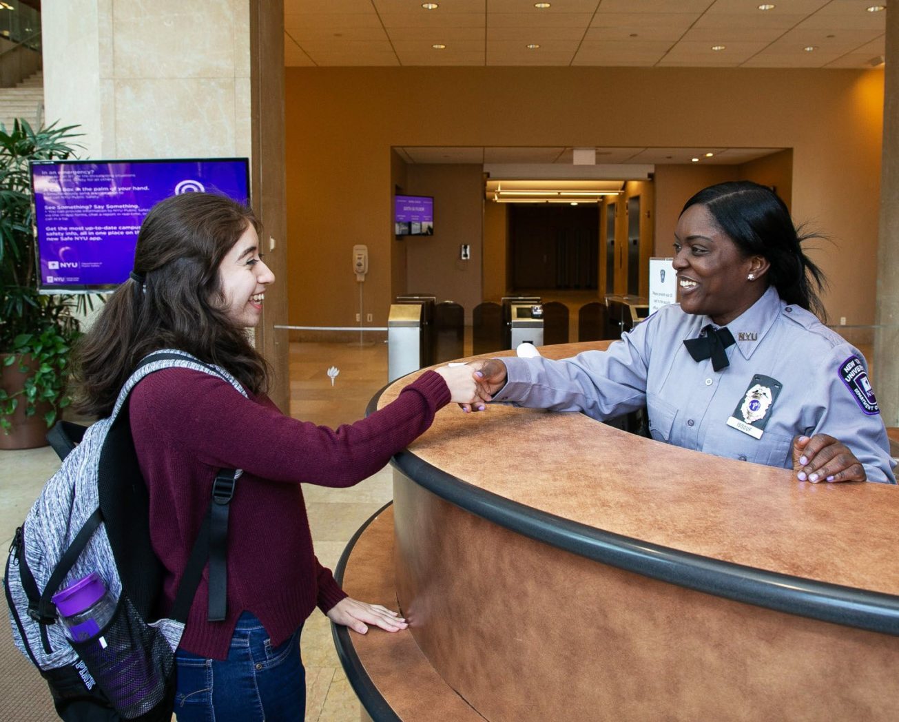 NYU student shaking hands with a Public safety officer who is sitting behind their desk