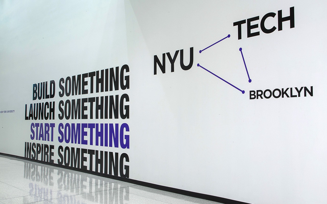 Wall graphics featuring the words “NYU,” “Tech,” and “Brooklyn” connected by lines forming a triangle. The words “Build Something. Launch Something. Start Something. Inspire Something” appear to the left of the triangle.