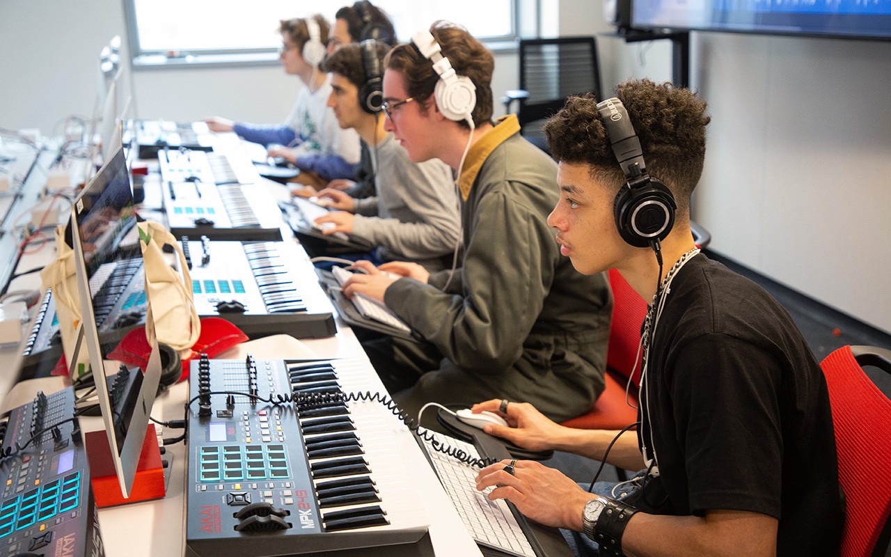 Students working on musical keyboards connected to computers in an audio editing class.